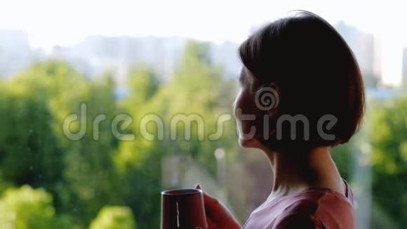 女人站在窗前喝咖啡或茶视频的预览图