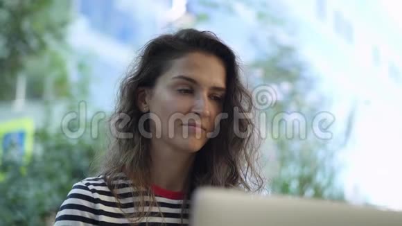 一位严肃的年轻女士在夏天的咖啡馆里看着笔记本电脑屏幕视频的预览图