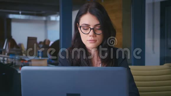 漂亮的年轻女商人戴着眼镜在现代办公室里用笔记本电脑工作视频的预览图