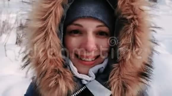 穿着皮衣帽的年轻美女在雪天的冬季城市公园里与视频连接和行走视频的预览图