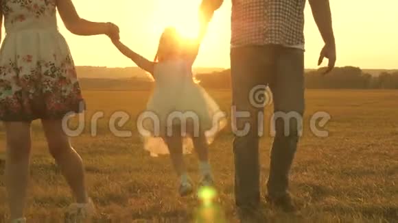 小女儿在太阳的背景下牵着爸爸和妈妈的手在公园里跳跃家庭观念孩子玩爸爸视频的预览图
