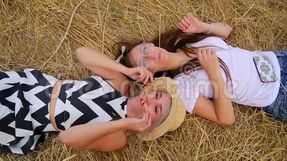两个可爱的积极女孩的特写镜头金发和黑发的傻瓜躺在金发上大笑视频的预览图