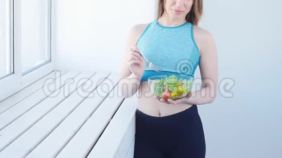 健康食品概念快乐的女人在白色的室内锻炼后吃健康的绿色沙拉视频的预览图