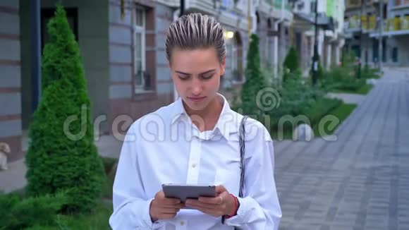 年轻的现代女性站在街上敲着平板电脑看着摄像机交流观念城市观念视频的预览图