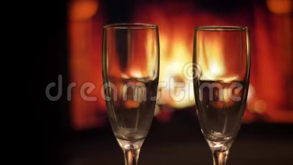两个空酒杯的特写镜头背景是室内黑暗中带火焰的温馨壁炉视频的预览图