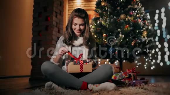 一个漂亮的女孩正在一个装饰得很好的客厅里打开一个坐在地板上的圣诞礼物视频的预览图