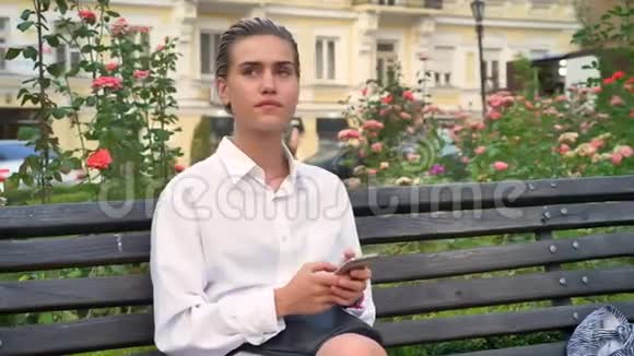 年轻的现代女性坐在街边的长椅上白天四处张望在智能手机上输入信息视频的预览图