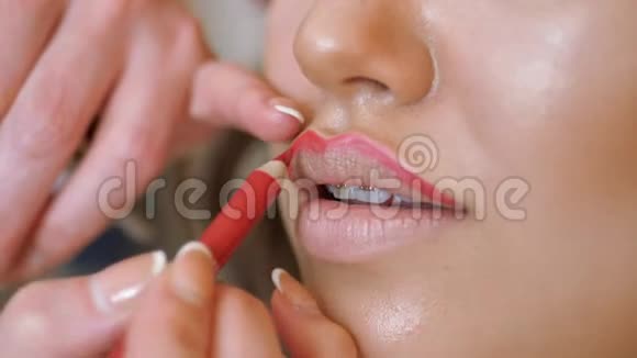 化妆师和模特一起工作造型师用红色铅笔画出模型嘴唇的轮廓视频的预览图