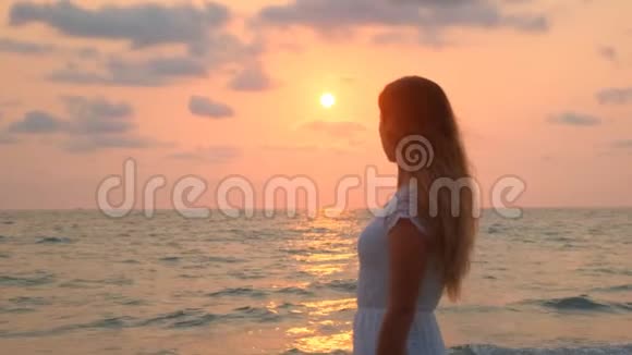 穿着白裙子的年轻漂亮女孩在海滩上散步海洋视频的预览图