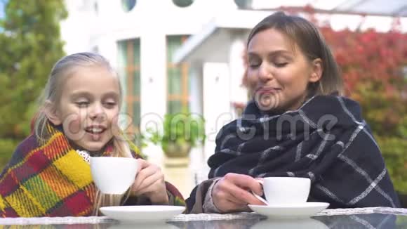 母亲和孩子裹着格子呢喝着温暖的茶享受着秋天的早晨视频的预览图