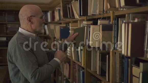 高级教授正在寻找书籍在室内沿着图书馆散步视频的预览图