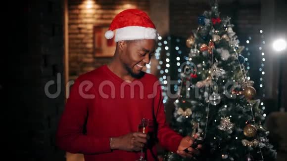一个拿着一杯香槟的帅哥在笑在家里的室内看圣诞节电话里的照片视频的预览图