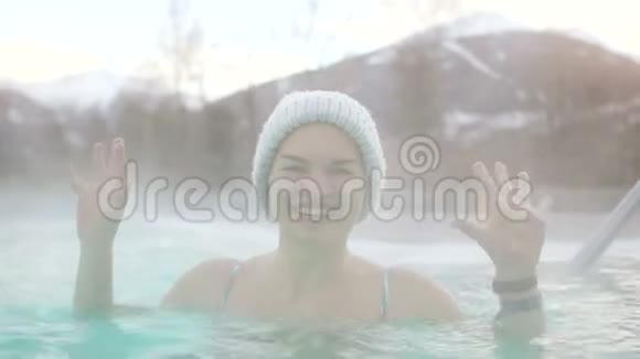 头上戴着针织帽子的年轻女孩在一个炎热的室外游泳池里洗澡女孩举起双手视频的预览图