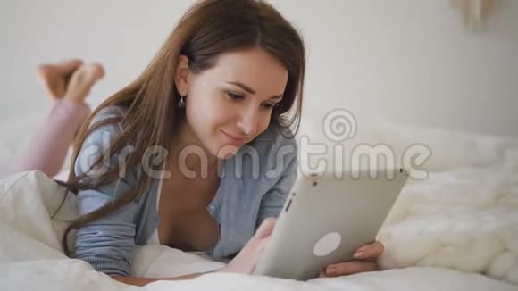 美丽的女人棕色长发躺在床上铺着白色床单交流着视频的预览图