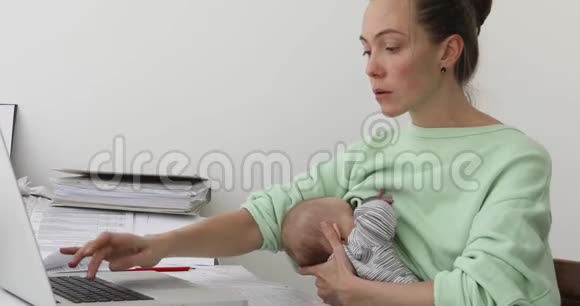 女人喂养婴儿和使用笔记本电脑视频的预览图