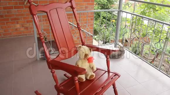 一只老式玩具熊坐在一个开放的阳台上的摇椅上摇摆夏季蔬菜视频的预览图