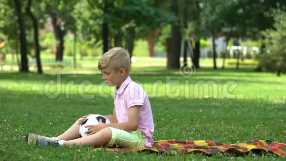 悲伤的男孩坐在公园里扔球缺乏朋友欺凌的受害者视频的预览图