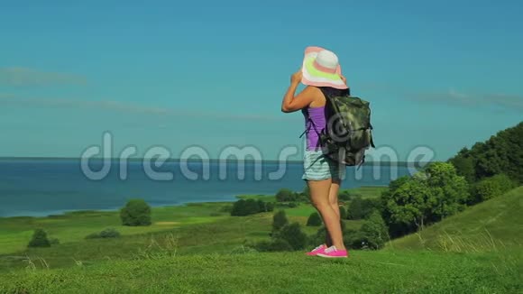 一个戴着草帽背着背包的女人站在山上欣赏下面的湖水从后面射击视频的预览图