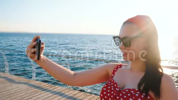 漂亮的女人在海边用黑色手机穿复古红色圆点连衣裙的女孩自拍视频的预览图