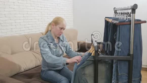 坐在沙发上的女人检查挂在衣架上的一套牛仔服装视频的预览图