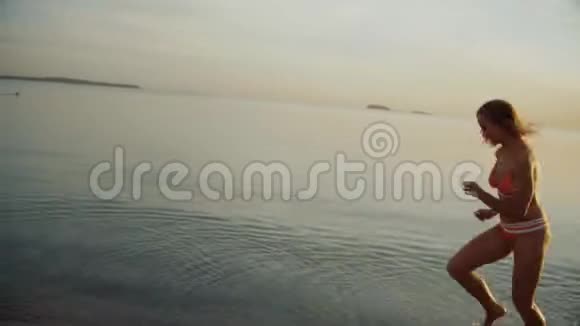 美丽的女孩沿着海岸线奔跑黄昏时分瘦小的女人在傍晚跑步自由视频的预览图