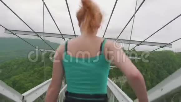 两个赤着双腿戴着3D眼镜的白种人女孩正沿着绿色森林上的高悬桥走着视频的预览图