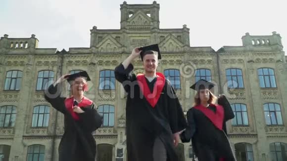 快乐的学生穿着黑色和红色的壁炉在大学大楼前庆祝他们的毕业两个女孩视频的预览图