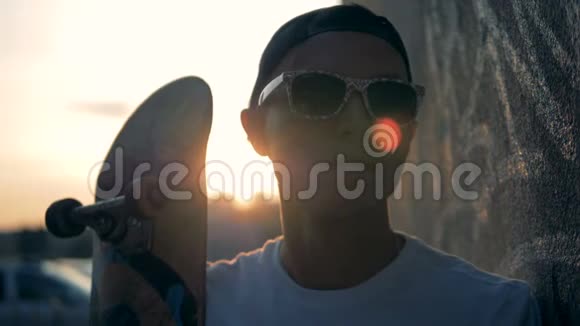青少年站在日落背景上带着滑板特写视频的预览图