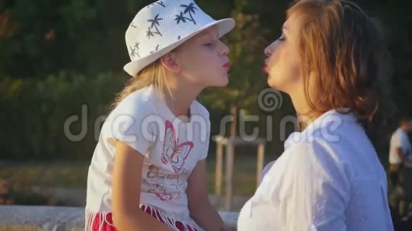 妈妈在她女儿旁边欣赏城市日落戴着可爱帽子的可爱的母女被傍晚的阳光照亮视频的预览图