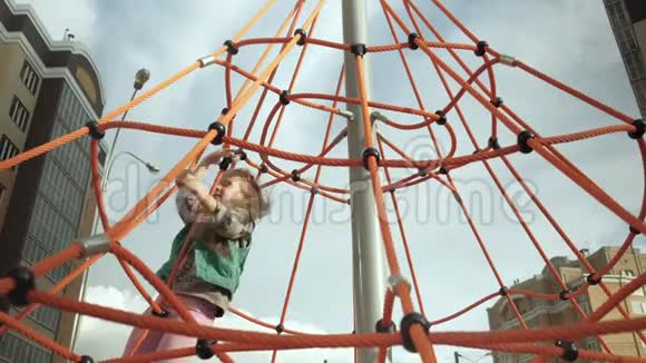一个孩子在户外操场上爬上一根绳子的水平杆视频的预览图