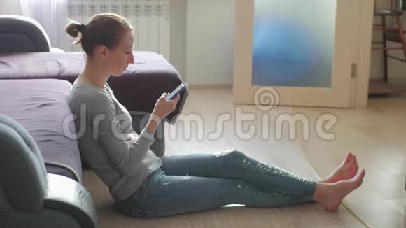 微笑的年轻女子使用手机而坐在地板上在家里视频的预览图