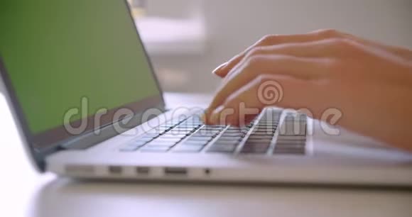 年轻的高加索女商人在室内办公室用绿色彩色屏幕在笔记本电脑上打字的特写照片视频的预览图