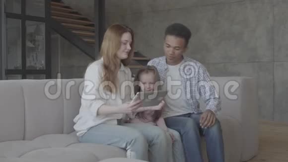 美丽的年轻国际家庭在家非裔美国人男人白种人女人和小女孩坐在沙发上视频的预览图