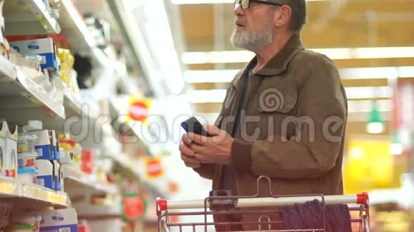 超市里的一位老人正试图在奶制品部门挑选奶酪微笑着看着智能手机视频的预览图