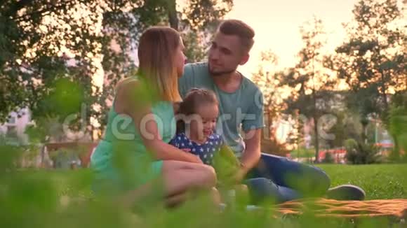 夏天一家人坐在公园的地毯上父母亲吻放松观念视频的预览图