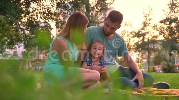 夏天一家人坐在公园的地毯上女儿在玩耍放松观念视频的预览图