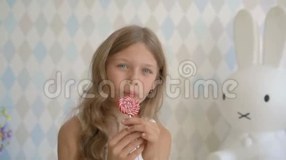 漂亮的小女孩带着棒棒糖快乐的小女孩在家吃糖果视频的预览图
