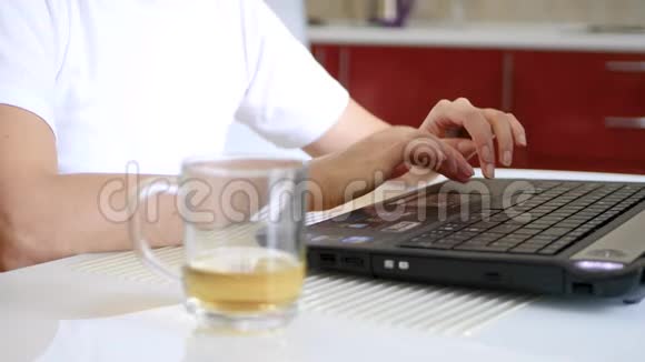 一个女孩的手在笔记本电脑键盘上打字笔记本电脑旁边是一杯茶视频的预览图