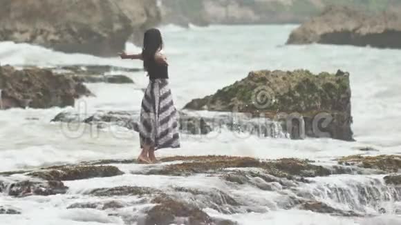 一个年轻的印度尼西亚女孩很高兴在巴厘岛的岩石海岸上掀起巨浪视频的预览图