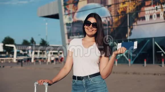 微笑的年轻女子手持护照手中拿着机票站在机场或火车站附近的画像视频的预览图