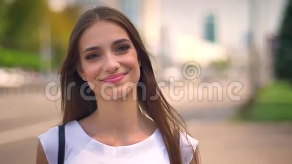 美丽的女人在夏天的白天站在公共汽车站看着镜头微笑着背景模糊的道路视频的预览图