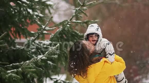 八个月大的孩子和他妈妈一起散步女人把婴儿帽伸直在云杉的背景下下雪视频的预览图