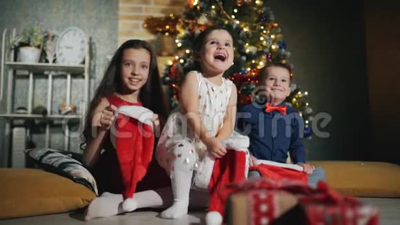 快乐的孩子头上戴着圣诞老人的帽子新年之夜在圣诞树脚下视频的预览图
