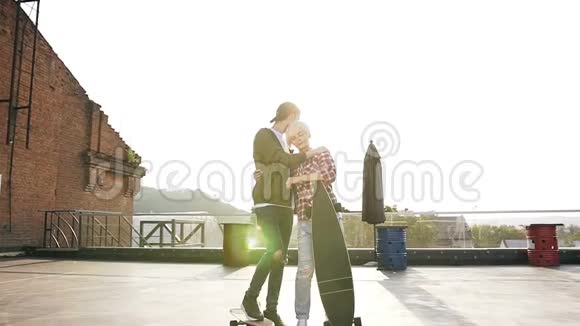 在日落时分一对年轻迷人的情侣在露台建筑的屋顶上用滑板行走他和他的视频的预览图