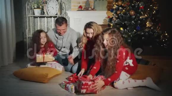 四个人的幸福家庭正在打开圣诞礼物新年之夜在圣诞树脚下视频的预览图