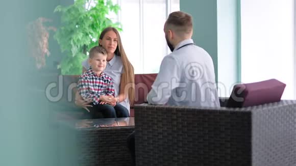 母亲跪着小儿子坐在椅子上和医生说话视频的预览图