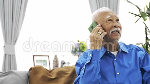 戴着白胡子的亚洲老人在家里用智能手机说话视频的预览图