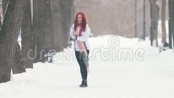 冬季公园一个开朗的女人一头鲜红的头发站在人行道上做一个雪球朝前扔去视频的预览图