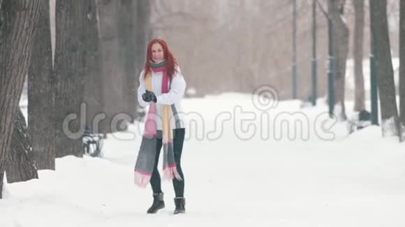 冬季公园一个留着鲜红头发的女人站在人行道上做一个雪球然后把它向前扔视频的预览图