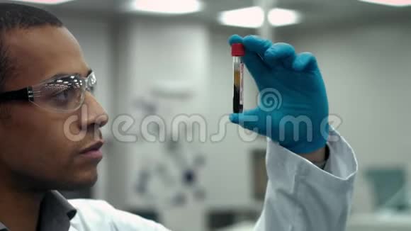 年轻的男科学家在实验室检查一个装满血液的试管视频的预览图